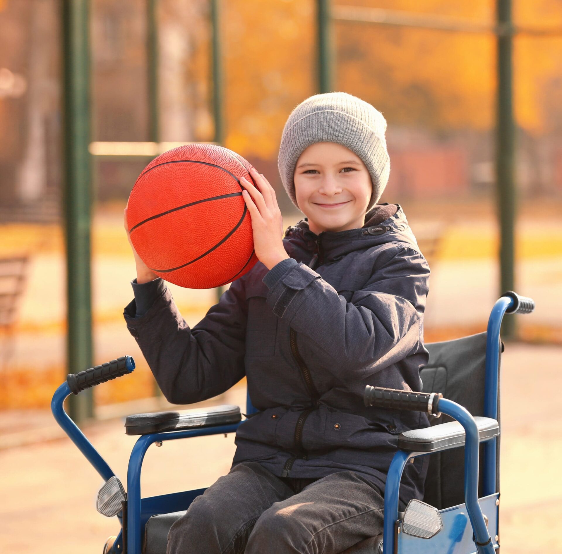 Smiling boy in a wheelchair holding a basketball outdoors